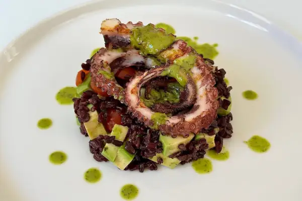 Delizioso polpo alla griglia su letto di riso venere, avocado e pomodorini, condito con salsa verde.