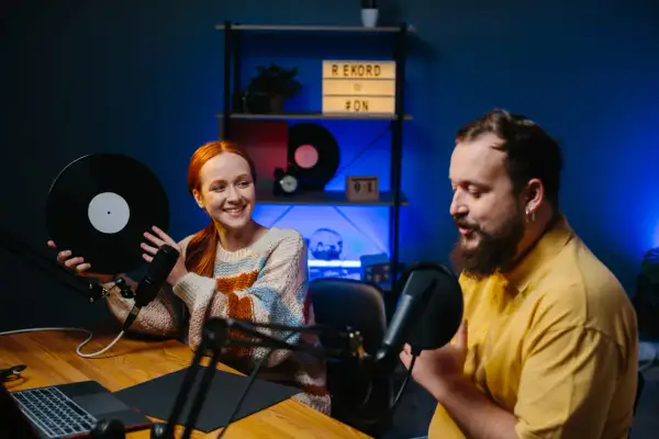 Coppia discute di come fare un podcast, lei tiene un vinile, lui parla al microfono.