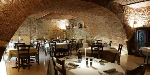 Interno di un ristorante con tavoli apparecchiati, soffitto a volta in mattoni e pareti in pietra. Un'atmosfera accogliente, ideale per scoprire i migliori ristoranti di Verona.