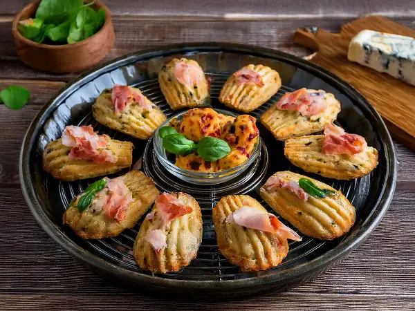 Délicieuses madeleines salées pour apéritif, garnies de jambon cru et de basilic. Parfaites pour une recette facile et gourmande.
