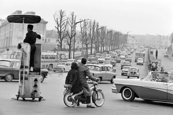 Un agent régule la circulation sur ce qui semble être la première autoroute de France, avec une file de voitures et un couple sur une mobylette.