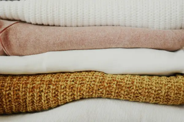 Pile di maglioni color pastello e ocra. Scopri come togliere elettricità dai vestiti per un comfort ottimale.