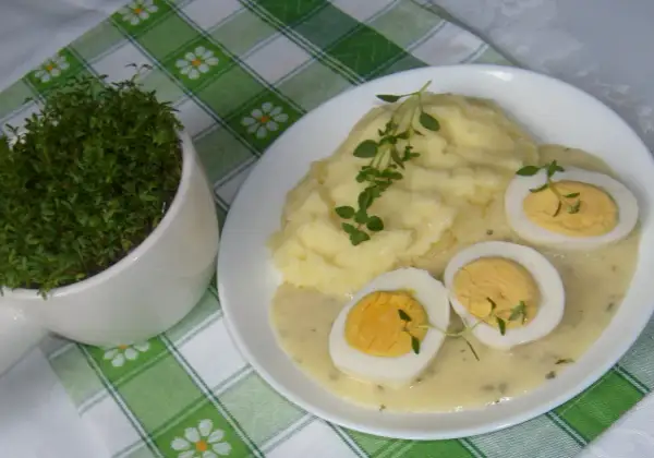 Pyszne ziemniaki puree z jajkami w sosie chrzanowym na ciepło, udekorowane gałązkami ziół. Obok doniczka ze świeżą rzeżuchą.