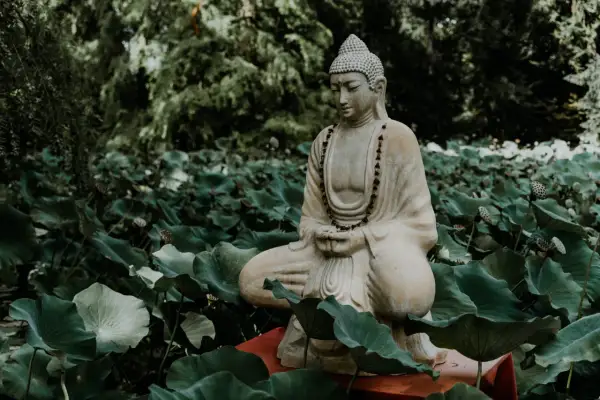 Kamienna figura Buddy w pozycji medytacyjnej, otoczona liśćmi lotosu.
