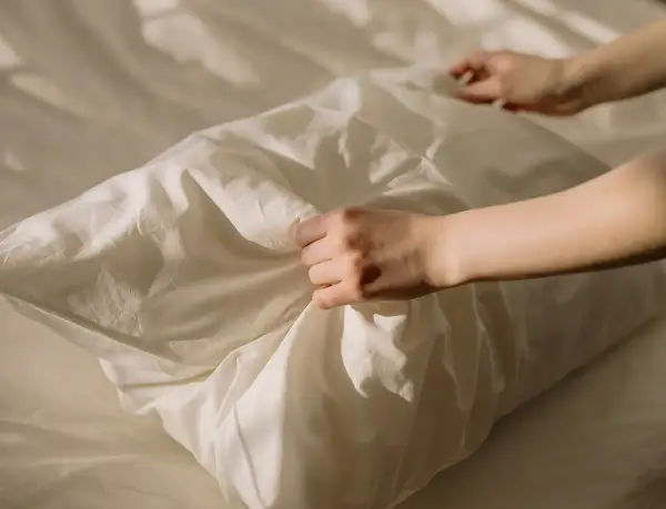 Manos arreglando una funda de almohada blanca, como si se preparara para blanquear fundas de almohadas amarillentas.