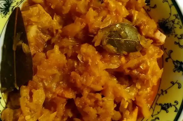 Pyszny bigos ze słodkiej kapusty, z dodatkiem liści laurowych, w żółtej misce z ozdobnym wzorem.