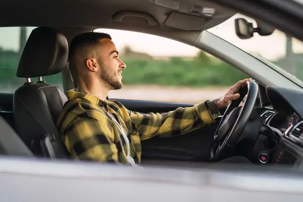 Joven sonriente conduce con las manos en el volante, promoviendo la seguridad al volante.