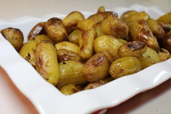 Un plat blanc rempli de pommes de terre nouvelles rôties, dorées et appétissantes.