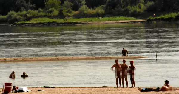 Ludzie opalają się i kąpią na piaszczystej plaży nad rzeką. To popularne miejsce, gdzie można spotkać plażę nudystów.