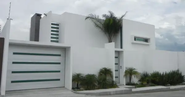 Casa moderna con líneas limpias y un estilo arquitectónico minimalista. Puerta de garaje blanca con detalles verdes.