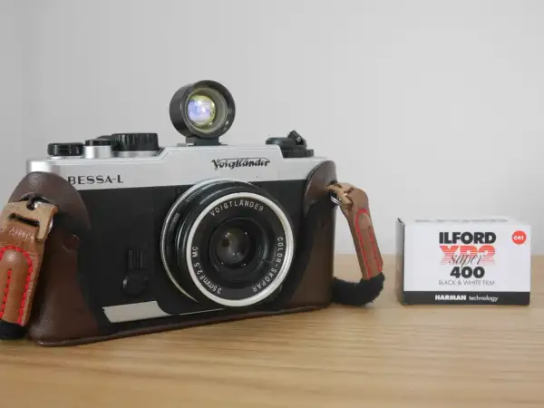 A silver and black Voigtlander Bessa-L camera in a brown leather case sits next to a box of Ilford XP2 Super 400 black and white film.