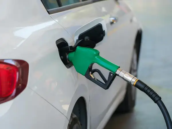 Zielona dysza dystrybutora paliwa wlewa płyn do białego samochodu. Dylemat: benzyna czy diesel?