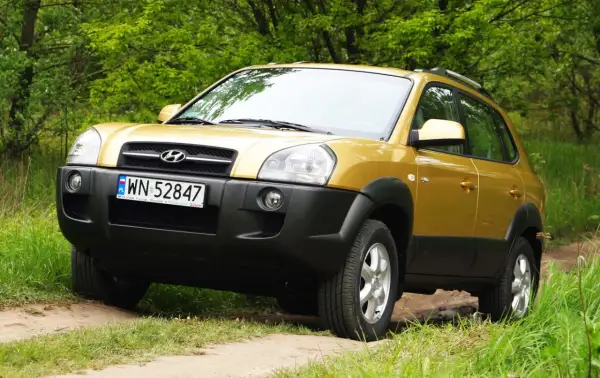 Złoty Hyundai Tucson 2007 na leśnej drodze, gotowy na przygodę.