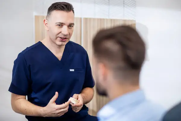 Dentysta w granatowym uniformie pokazuje pacjentowi model szczęki.