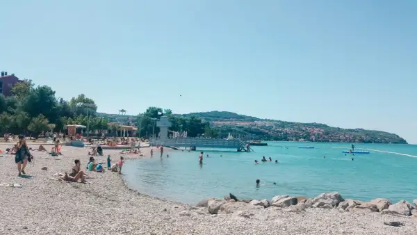 Słoneczna Słowenia zachwyca plażami. Ludzie kąpią się i opalają na kamienistym brzegu, ciesząc się błękitem Adriatyku.
