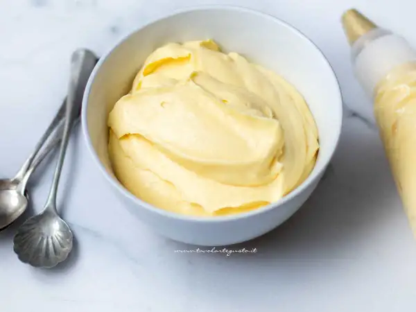 Crema chantilly soffice in una ciotola, pronta per decorare una torta. Accanto, cucchiaini d'argento e una sac à poche.