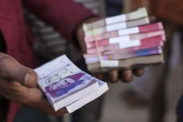 Dłonie trzymają stosy banknotów. W jednej dłoni widać wyraźnie banknot z portretem, to waluta Pakistanu.