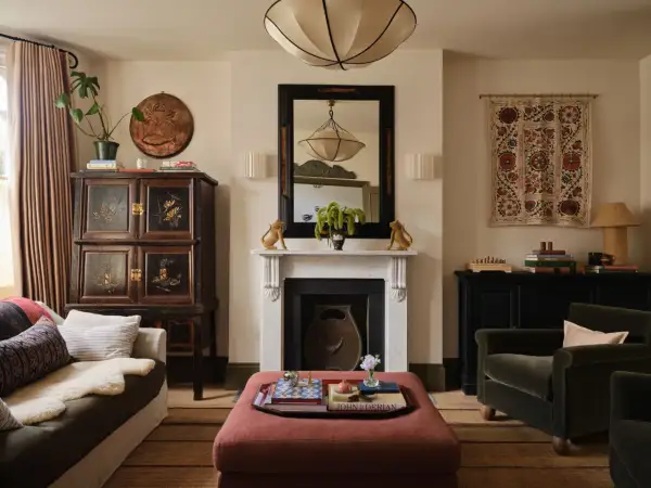 A living room with a plush ottoman, antique cabinet, and fireplace, showcasing a curated collection of minimalist home decor.