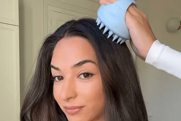 Mujer se masajea el cuero cabelludo con un cepillo azul para evitar cuando se cae mas el pelo.