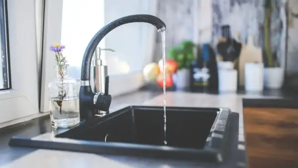 Ein Wasserhahn tropft in eine Spüle. Ein kleiner Strauß Blumen steht daneben. Dies könnte ein Hinweis auf den Kaltwasserverbrauch pro Person sein.