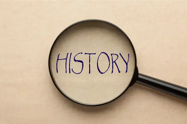 Lupa powiększająca napis "HISTORY" na papierze w kolorze beżowym.
