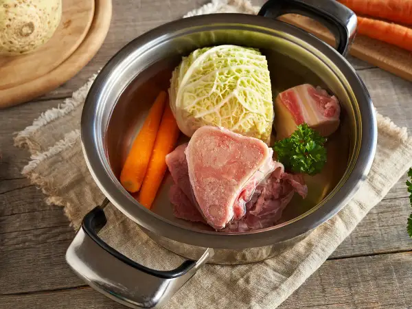 Une marmite de **potée au chou** avec des os de bœuf, des carottes, du chou et du persil, prête à mijoter.