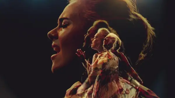 Adele śpiewa "Send My Love" w wielokrotnej ekspozycji, jej twarz i postać w sukni rozmywają się w mroku.
