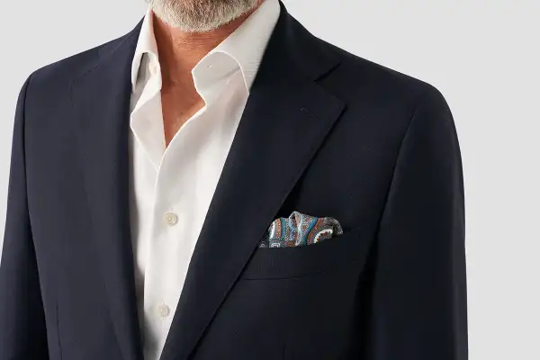 En mörk kavaj med en vit skjorta och en färgglad näsduk i bröstfickan.