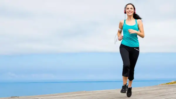 Mujer sonriente corriendo junto al mar, disfrutando de ejercicios para trabajar la autoestima y sentirse bien.