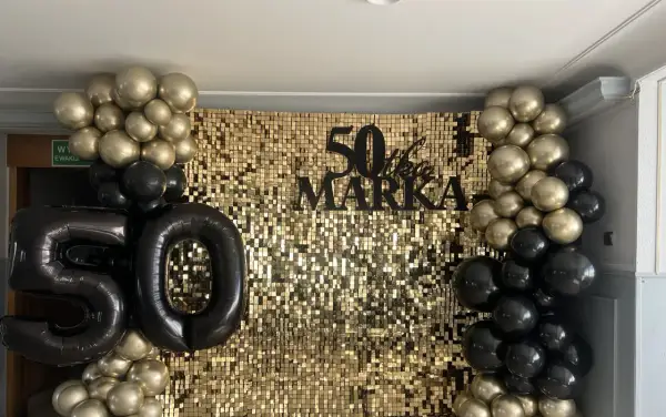 Złote i czarne balony otaczają błyszczące tło z napisem "50 lat Marka".