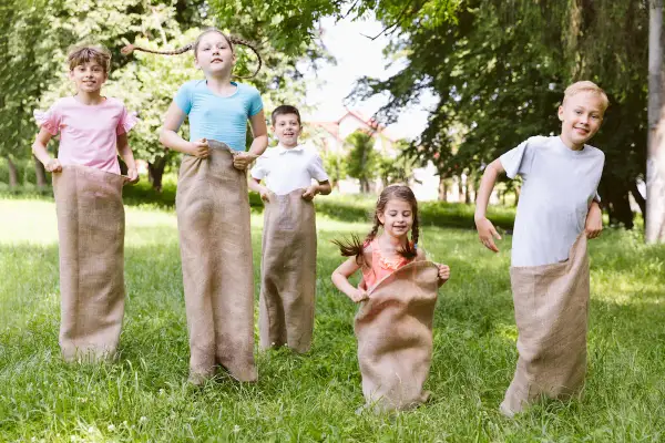 Niños compiten en carreras de sacos en un día soleado, disfrutando en familia de juegos al aire libre.