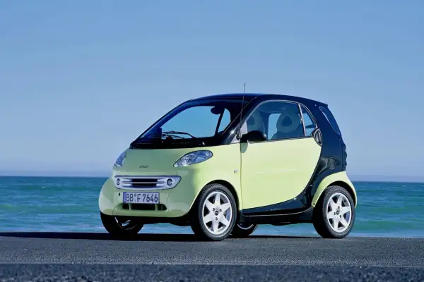 Jasnozielony smart fortwo 450 z czarnym dachem i czarnymi panelami bocznymi stoi nad błękitnym morzem.