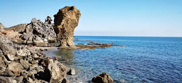 Rocas erosionadas y mar azul en la playa El Sombrerico. Una formación rocosa alta se alza como un guardián.