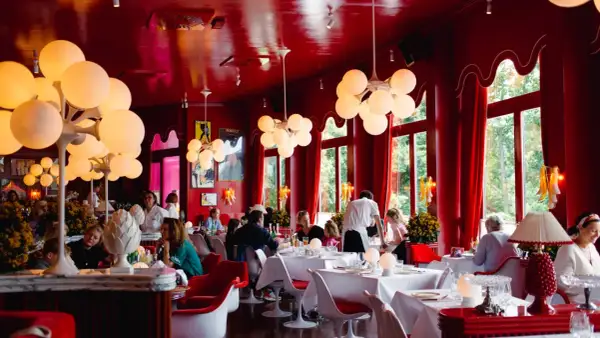 Ein lebhaftes **Cafe Berlin Mitte** mit roten Wänden, auffälligen Kugelleuchten und Gästen, die an weiß gedeckten Tischen sitzen.