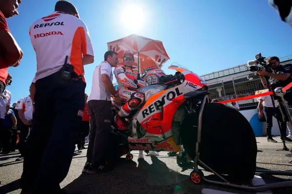 Piloto de MotoGP Repsol Honda listo en la parrilla de salida, bajo un sol radiante y rodeado de su equipo y cámaras.