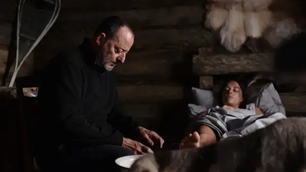 Jean Reno w "Cold Blood Legacy" obsada: mężczyzna pochyla się nad ranną kobietą w chatce.