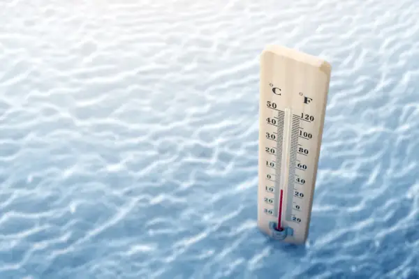 Drewniany termometr mierzy temperaturę wody na tle fal.
