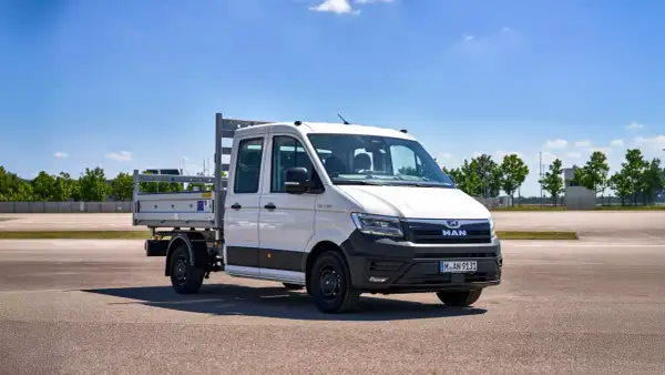 Camionnette MAN blanche avec plateau, prête pour le **c tuning** et le travail. Ciel bleu et verdure en arrière-plan.