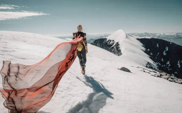 En kvinna med röd sjal vandrar på ett snötäckt berg. Emma Svensson fotograf.