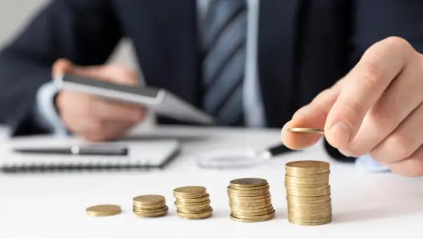 Dłoń kładzie monetę na rosnącej stercie, symbolizując zabezpieczenie alimentów i budowanie finansowej przyszłości.