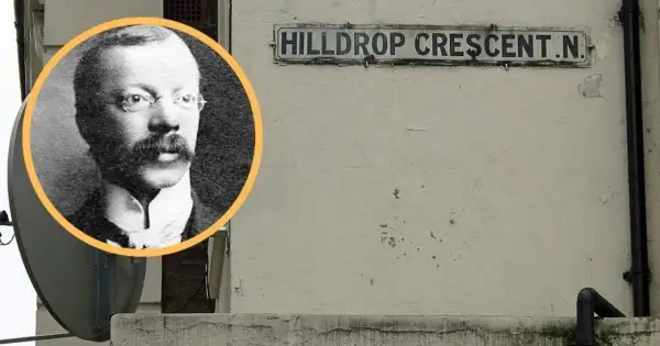 Czarno-białe zdjęcie mężczyzny w okularach i wąsach obok tabliczki z napisem "HILLDROP CRESCENT.N.".
