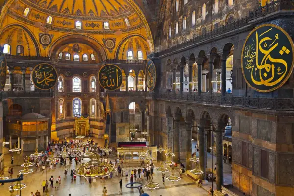 Wnętrze Hagia Sophia z wielkimi okrągłymi kaligrafiami, kopułą i tłumem turystów.