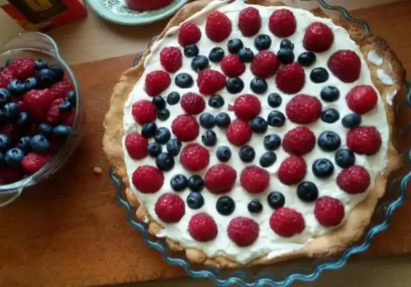 Pyszna tarta na słodko z malinami i borówkami, udekorowana kremem. Idealna na letnie popołudnie.