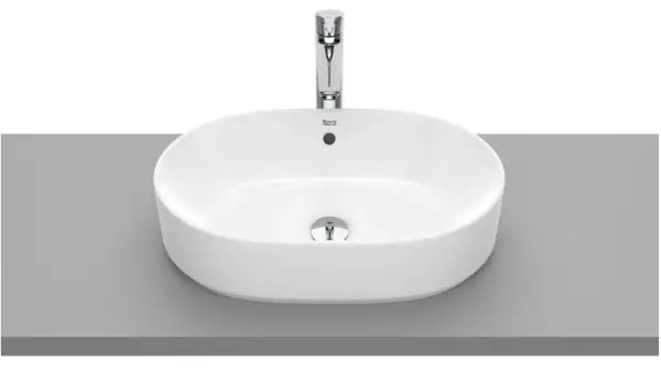 Elegancka, owalna umywalka nablatowa bez otworu na baterię, wykonana z białej ceramiki, z chromowanym korkiem.