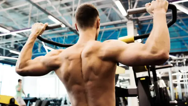 Un homme musclé effectue un tirage vertical, ses muscles dorsaux bien dessinés sous l'effort.
