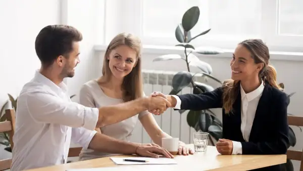 Accordo raggiunto: stretta di mano tra uomo e donna, con una collega sorridente. Si discute di stage e retribuzione minima.
