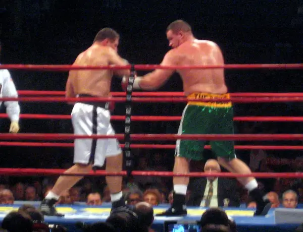 Two boxers in a ring, one in white shorts, the other in green. This bout adheres to the light heavyweight boxing weight limit.