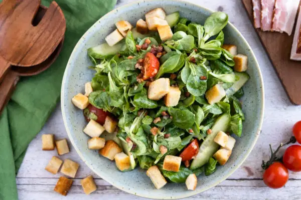 Frischer Feldsalat mit Speck und knusprigen Croutons, garniert mit Tomaten und Gurkenscheiben. Ein Genuss!