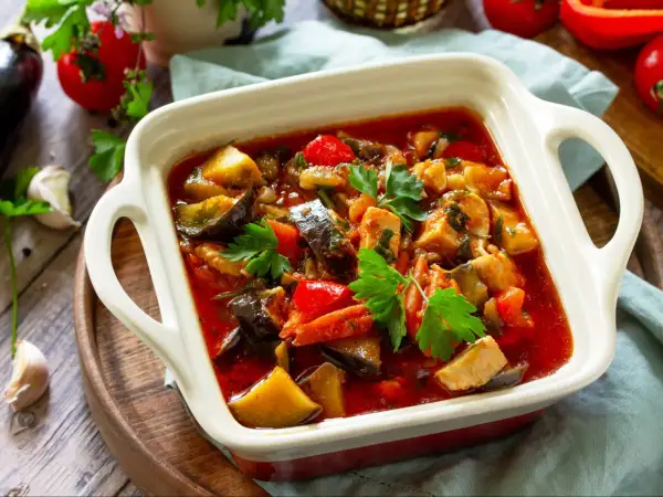 Pyszny gulasz z kurczaka z bakłażanem i papryką, udekorowany natką pietruszki. Aromatyczne danie w białej zapiekance.