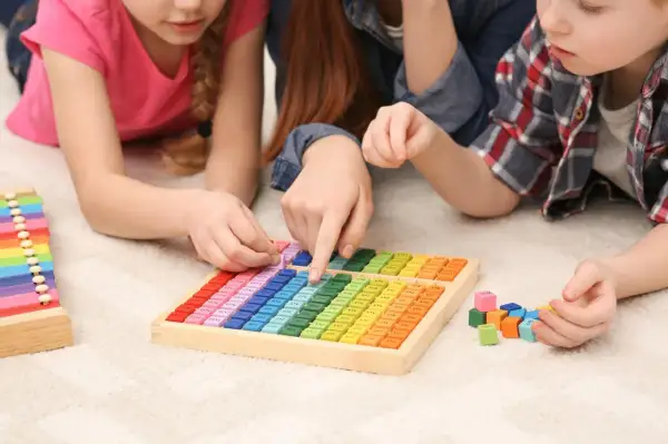 Kinder lernen spielerisch Mathematik im Kindergarten mit bunten Holzbausteinen und einer Multiplikationstafel.